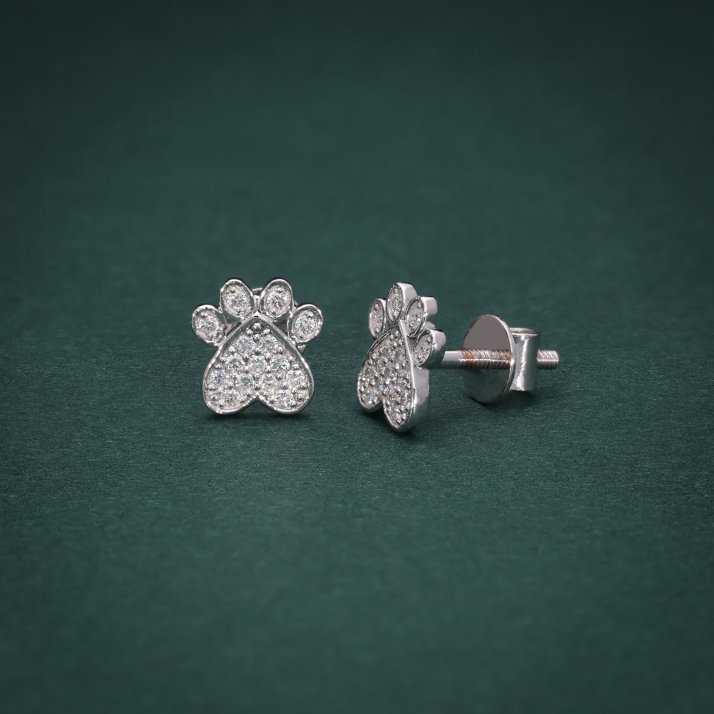 White gold stud earrings with a delicate paw design, accented with sparkling diamonds, symbolizing loyalty and love, shown on a green background.