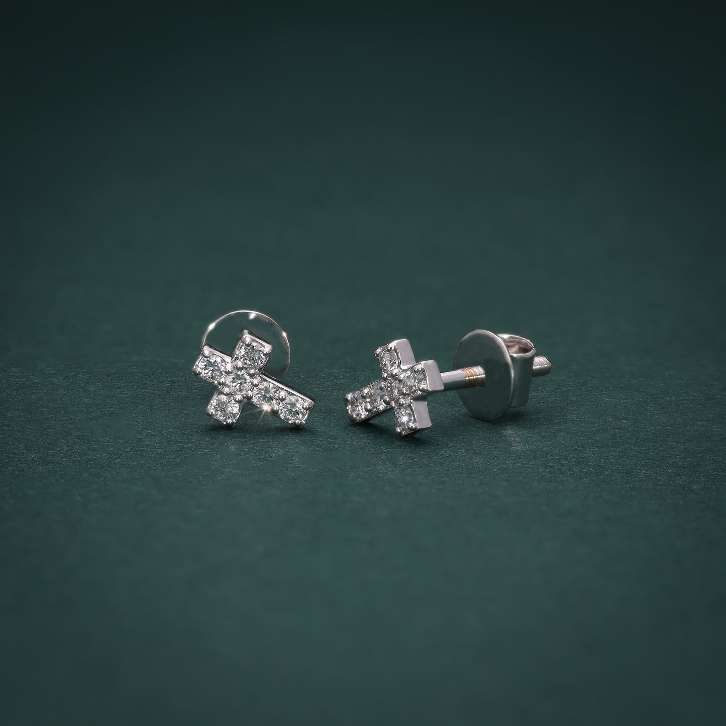 A pair of cross-shaped earrings adorned with lab-grown diamonds on a green background.