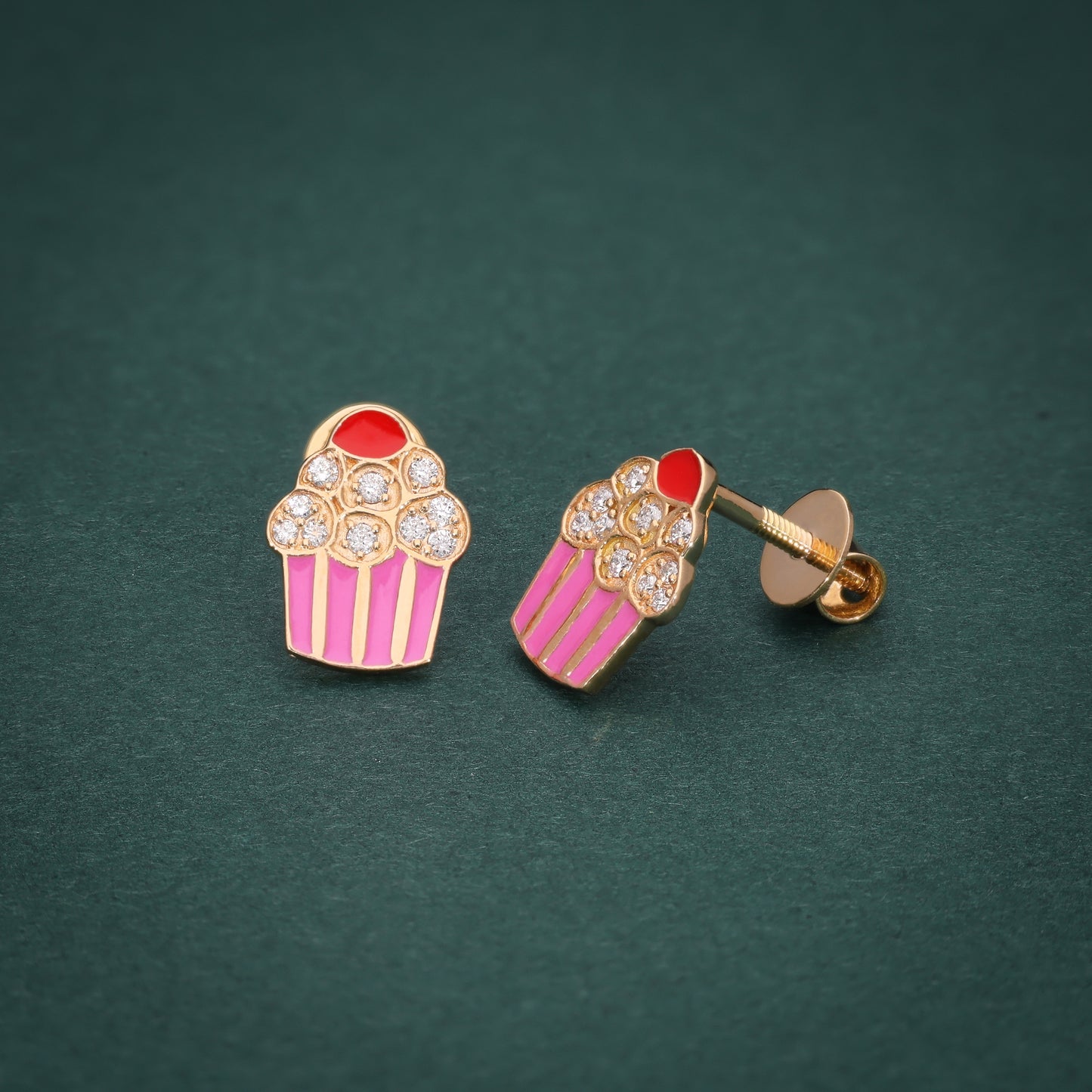 Cupcake-shaped stud earrings in gold with pink and red accents, adorned with sparkling diamonds, displayed on a green background.