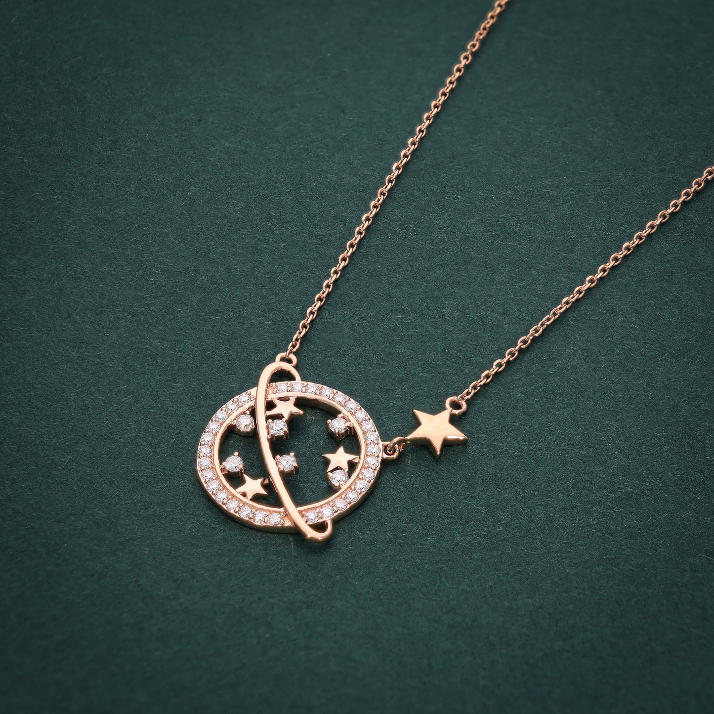 Rose gold necklace with a circular pendant featuring a diamond-studded ring and star motifs, accented by a dangling star charm on a dark green background