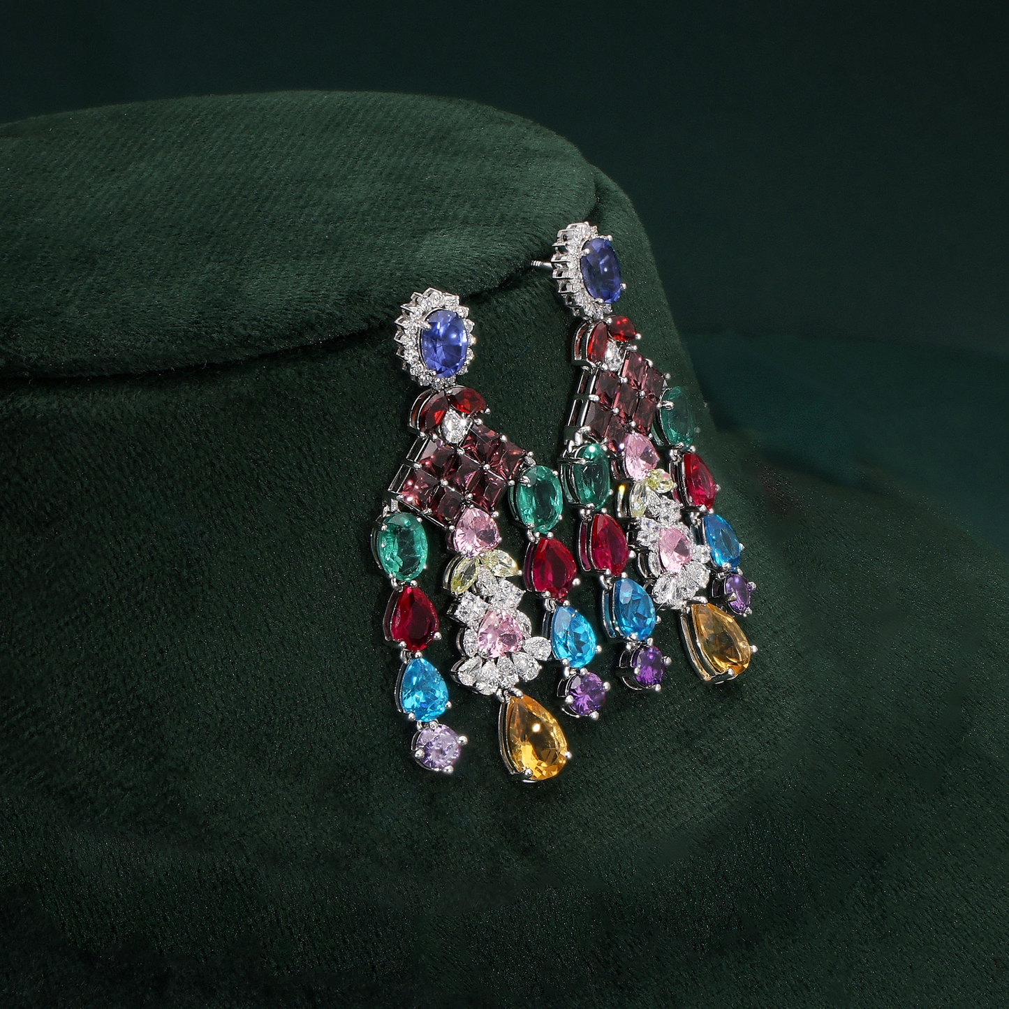 Multicolored gemstone earrings on a green velvet stand