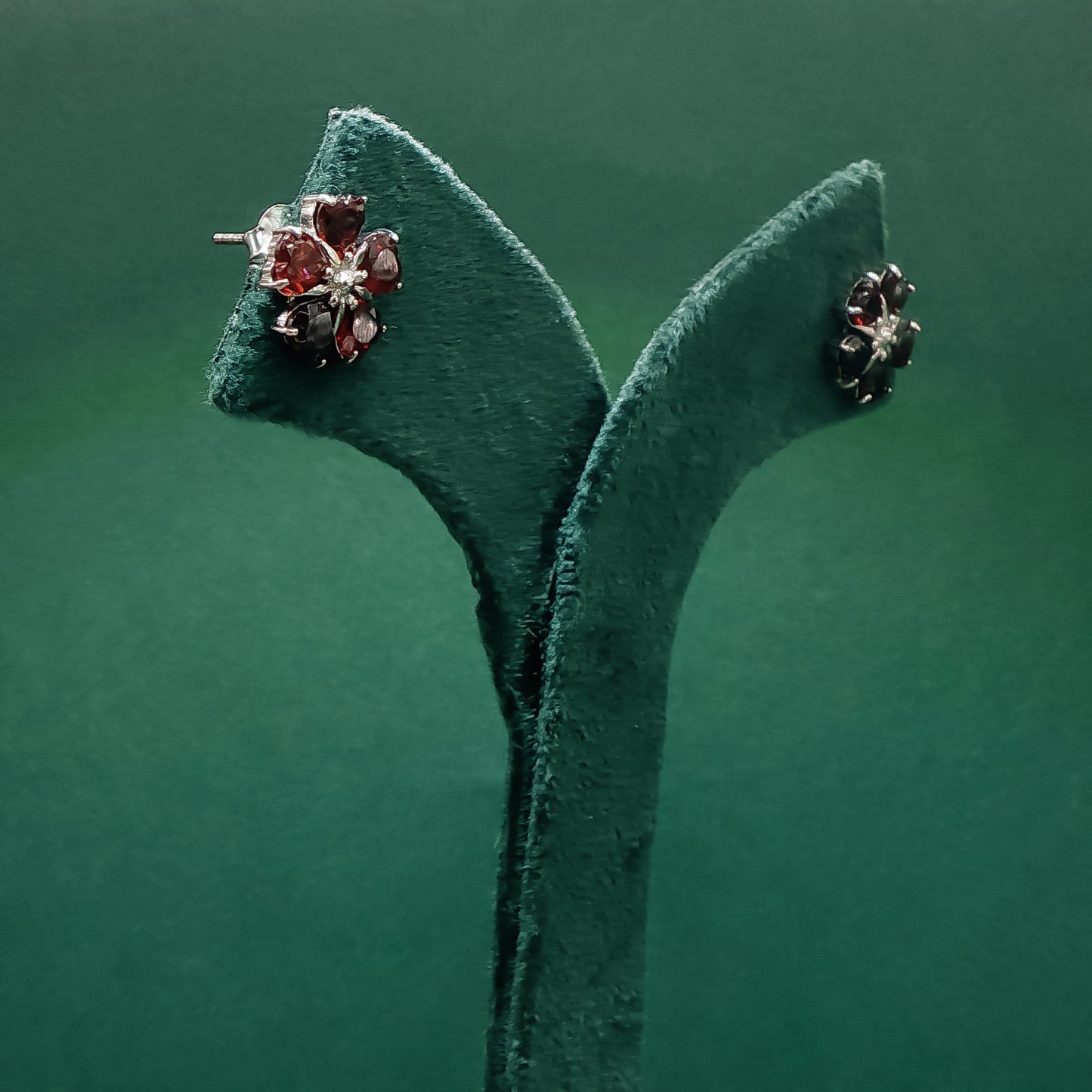 Pair of earrings on a green velvet stand against a green background