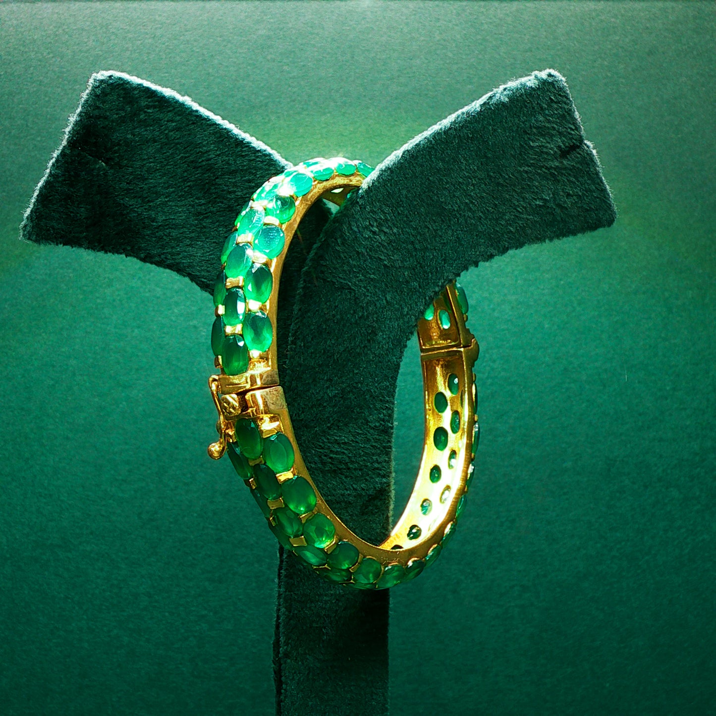 Gold hoop earrings with green gemstones on a green stand
