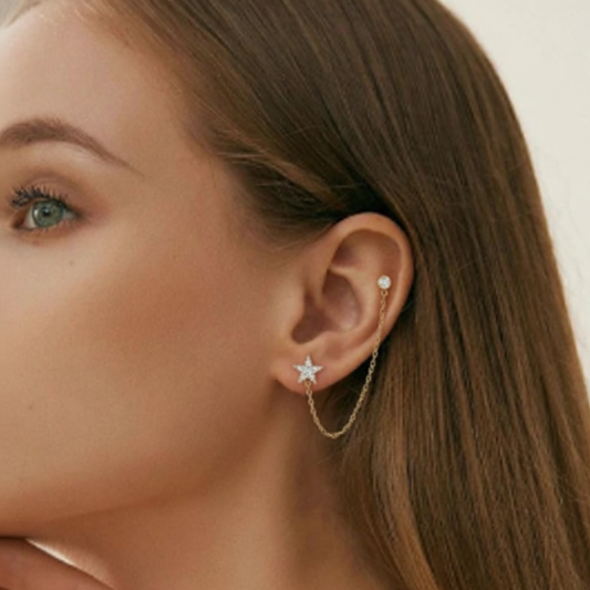 Close-up of a woman's ear wearing gold earrings with star and chain designs.