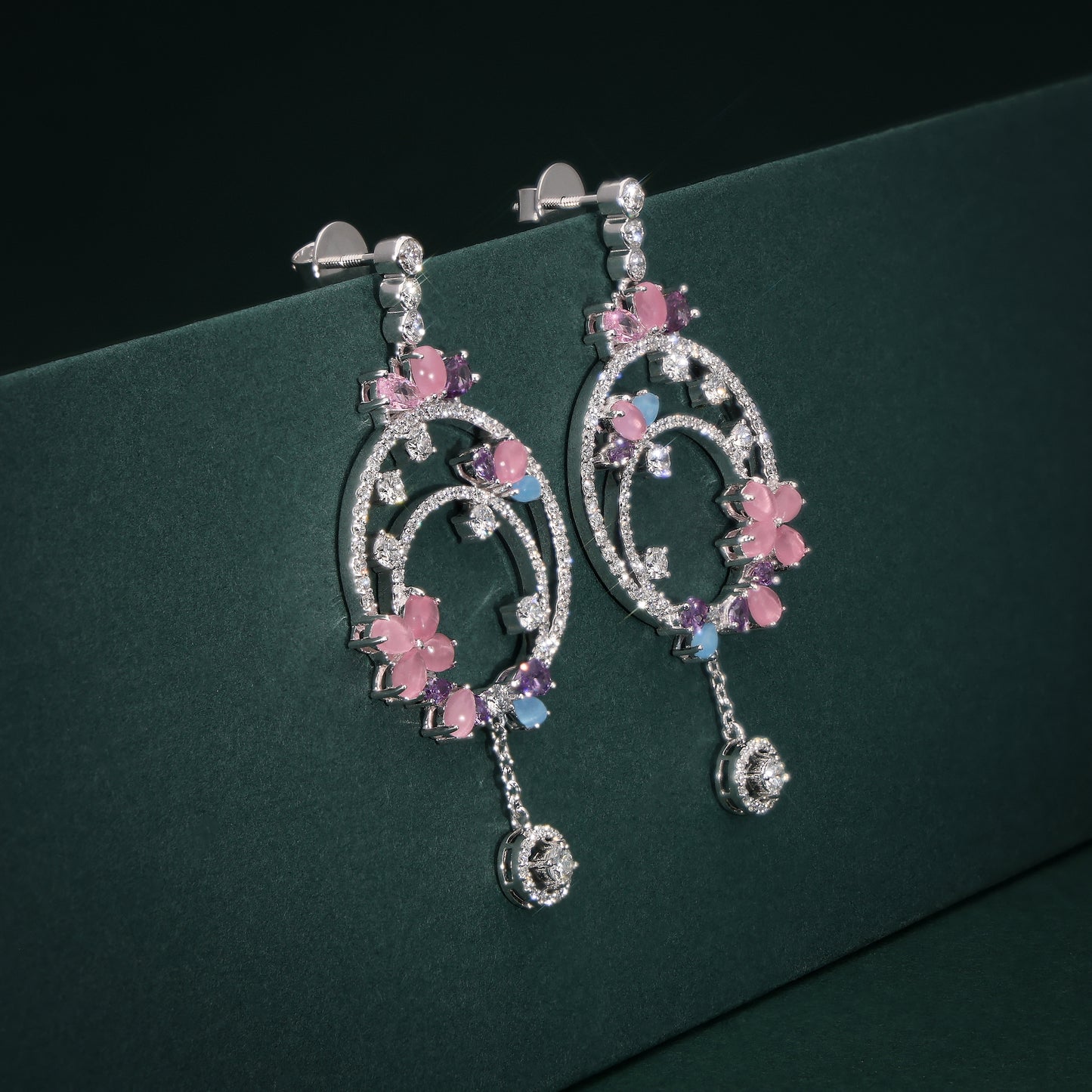 Pair of decorative earrings with pink floral elements on a green background