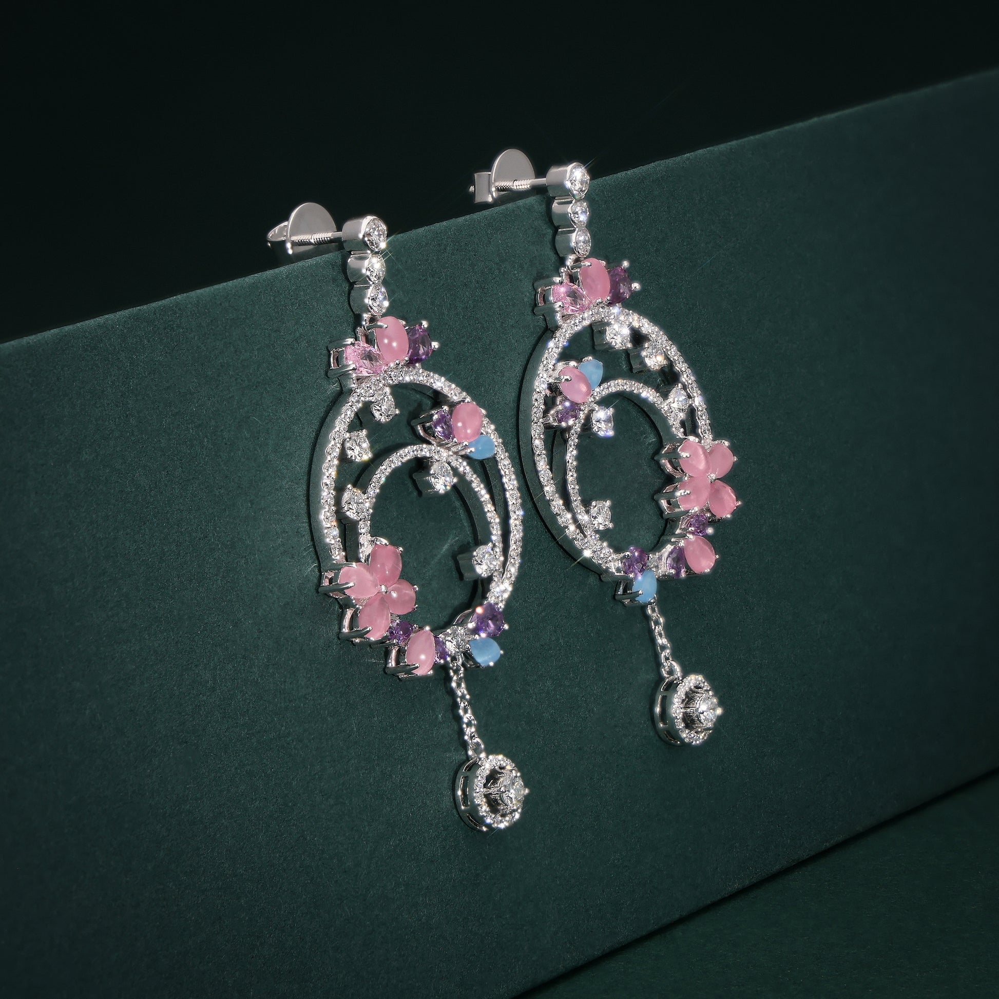 Pair of decorative earrings with pink floral elements on a green background