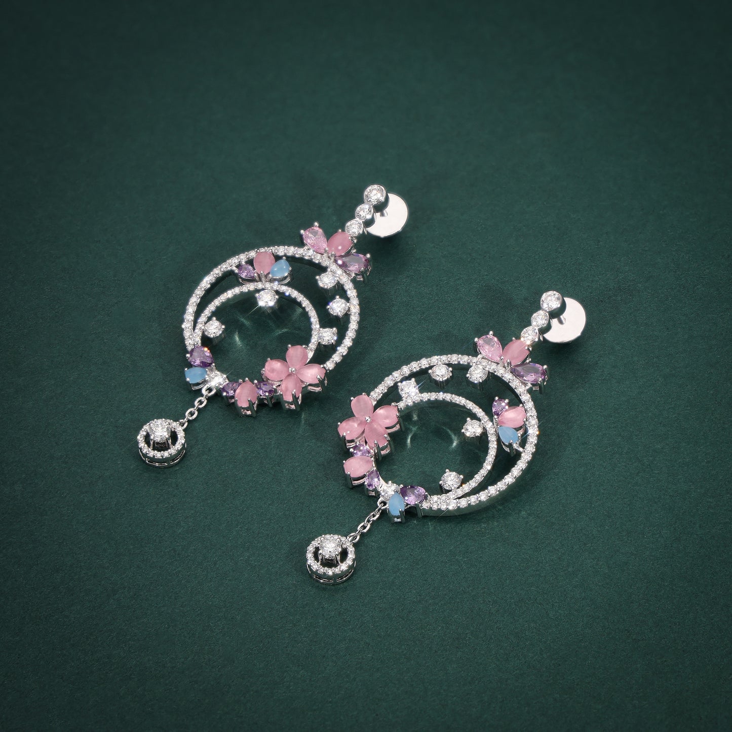 Pair of decorative earrings with pink floral elements on a green background