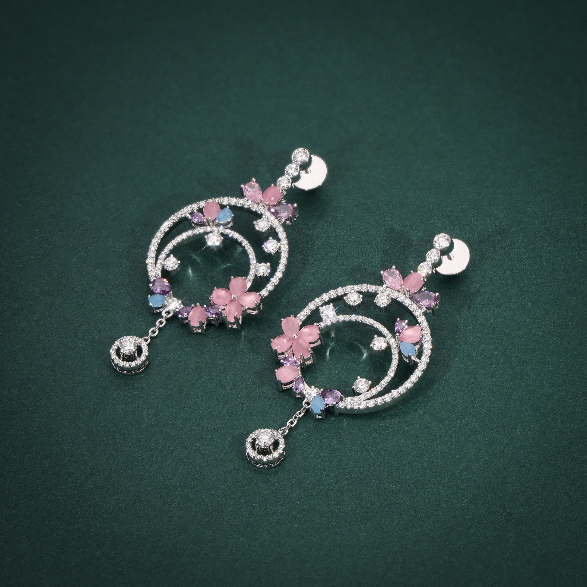 Pair of decorative earrings with pink floral elements on a green background
