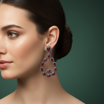 Close-up of a woman wearing a pair of red gemstone earrings against a green background