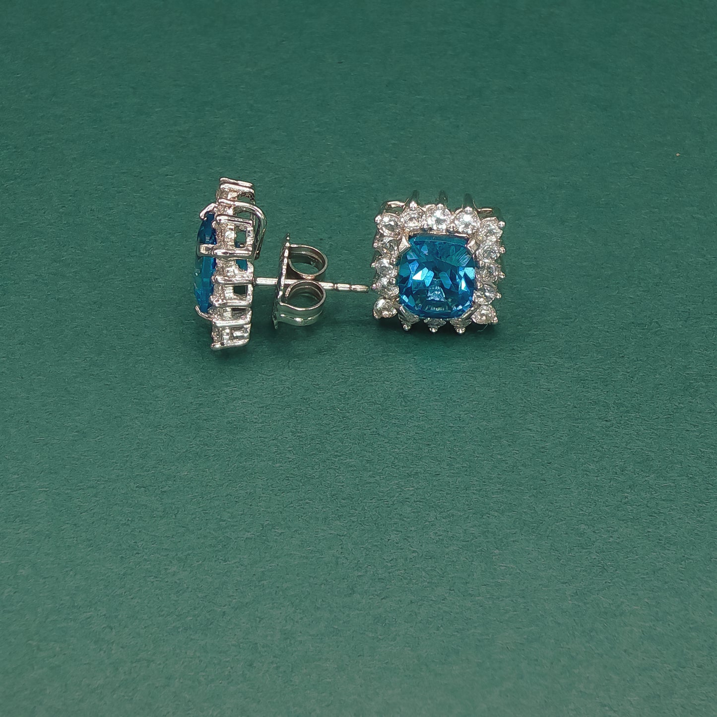 Pair of silver earrings with blue gemstones on a green background

