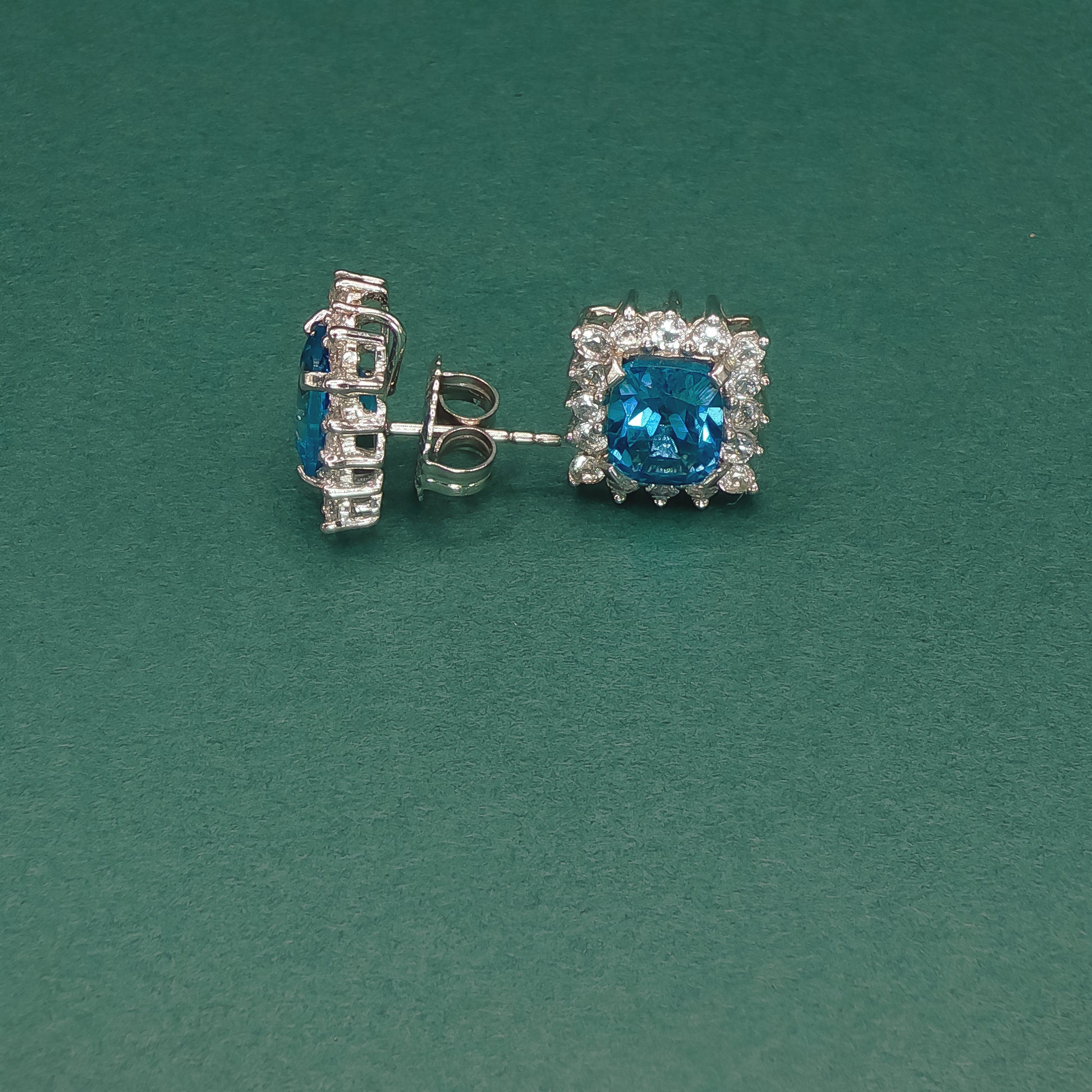 Pair of silver earrings with blue gemstones on a green background

