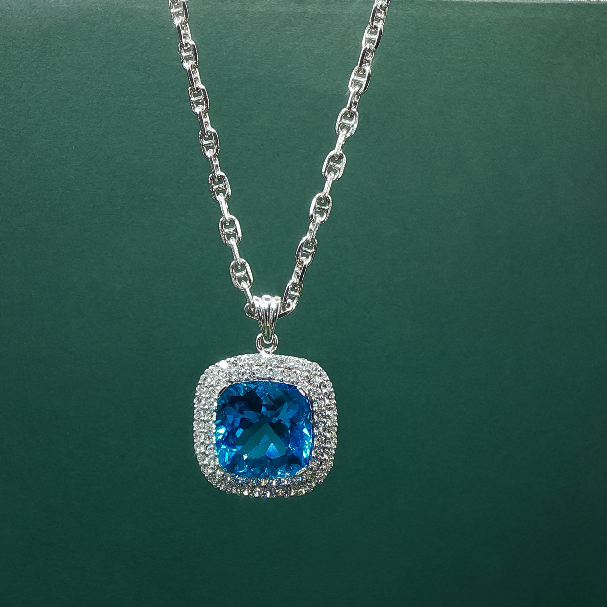 Silver necklace with a blue gemstone pendant on a green background


