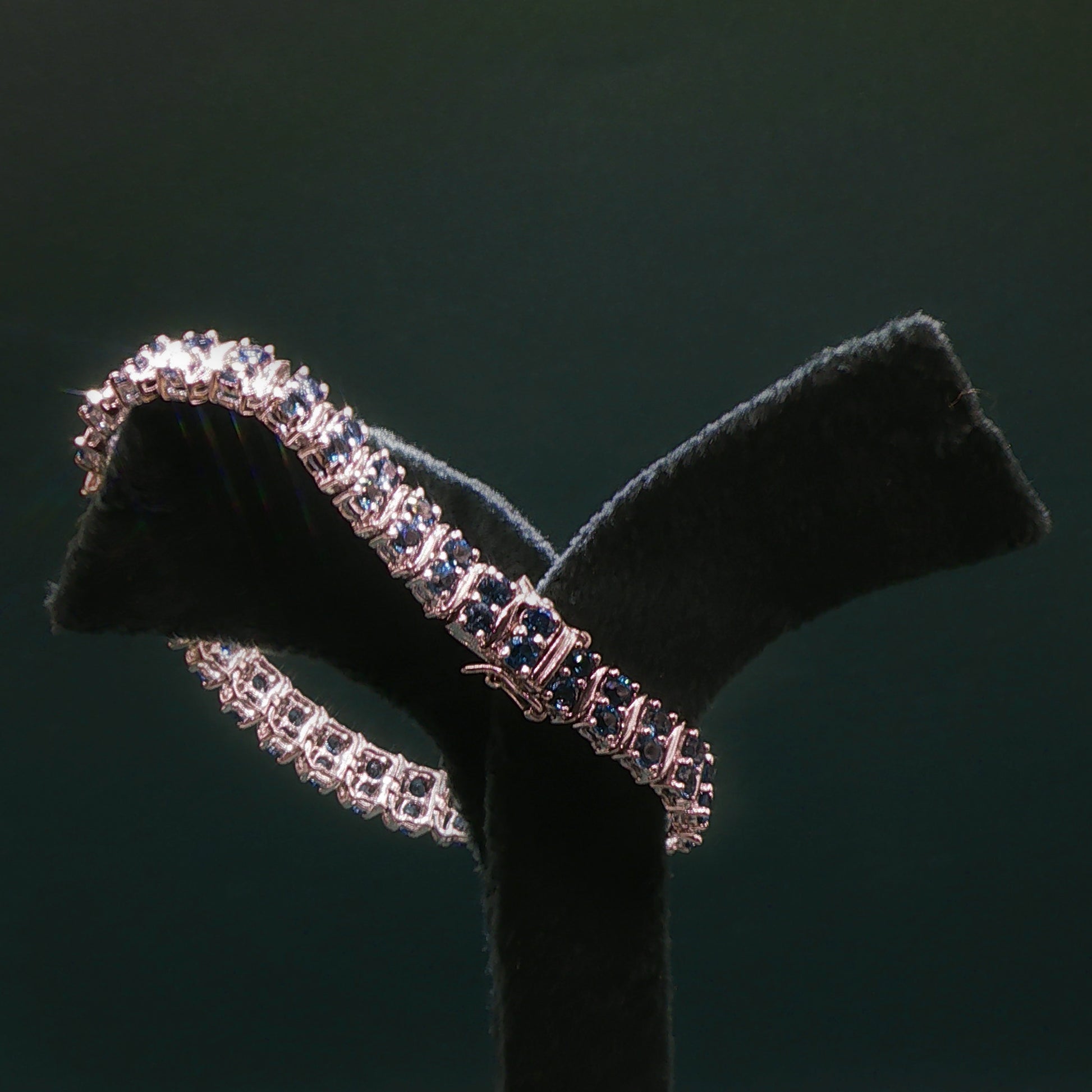 Silver bracelet with blue stones on a black stand against a dark background