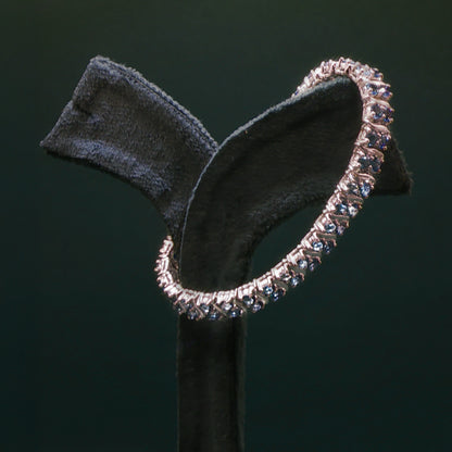 Silver hoop earring on a black stand against a dark background

