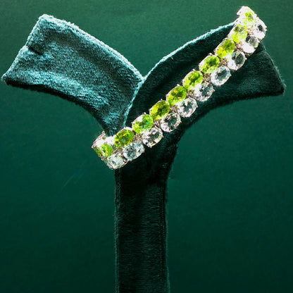 Bracelet with green and clear gemstones on a dark green background

