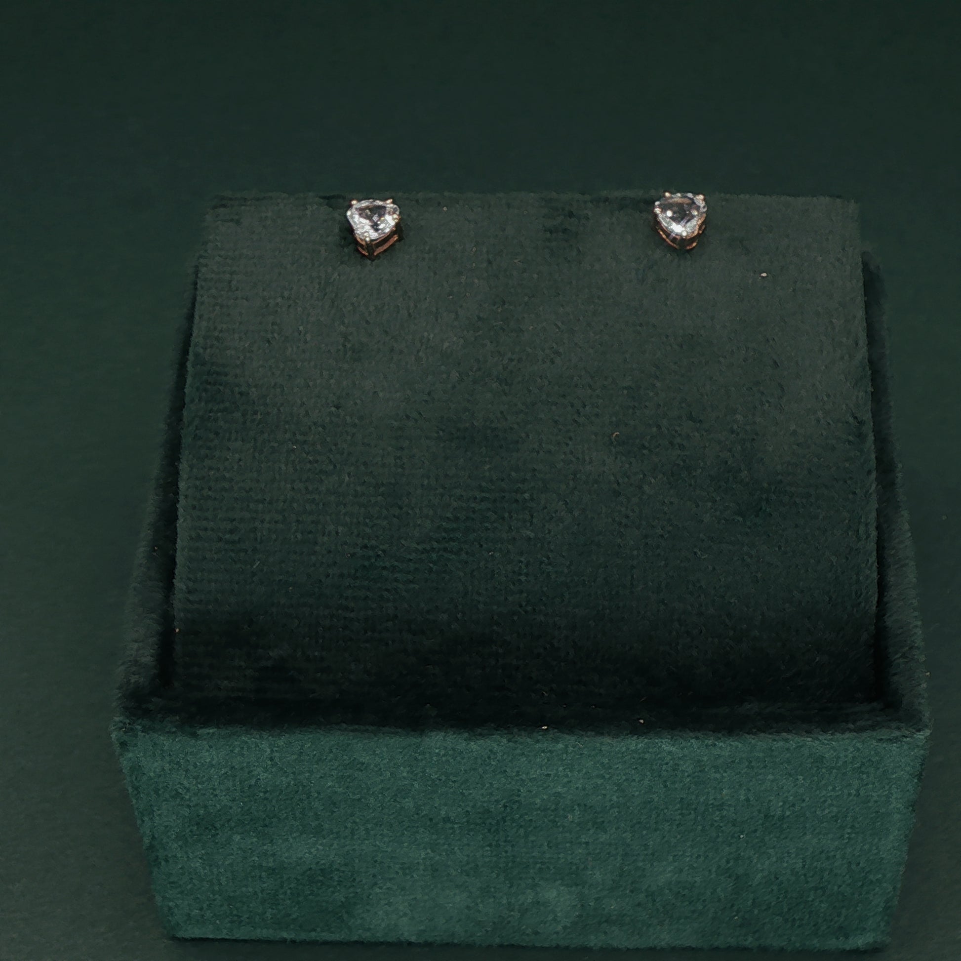 Heart-shaped earrings on a green velvet stand against a dark green background
