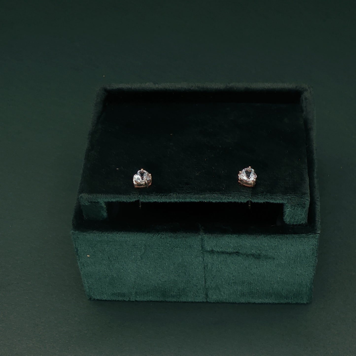 Pair of diamond stud earrings in a green velvet box on a dark background

