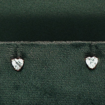 Heart-shaped diamond earrings on a dark green fabric background

