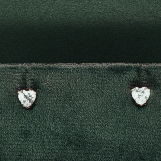 Heart-shaped diamond earrings on a dark green fabric background

