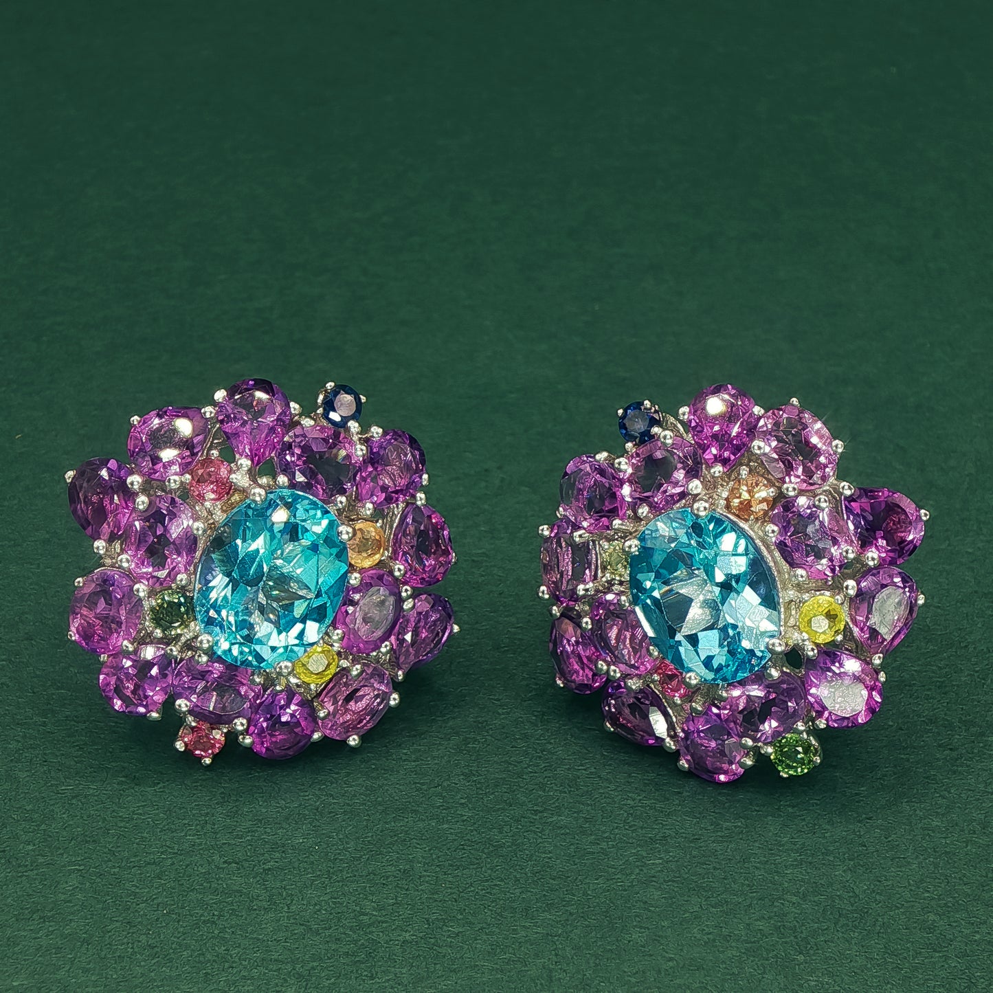 Colorful gemstone earrings on a dark green background

