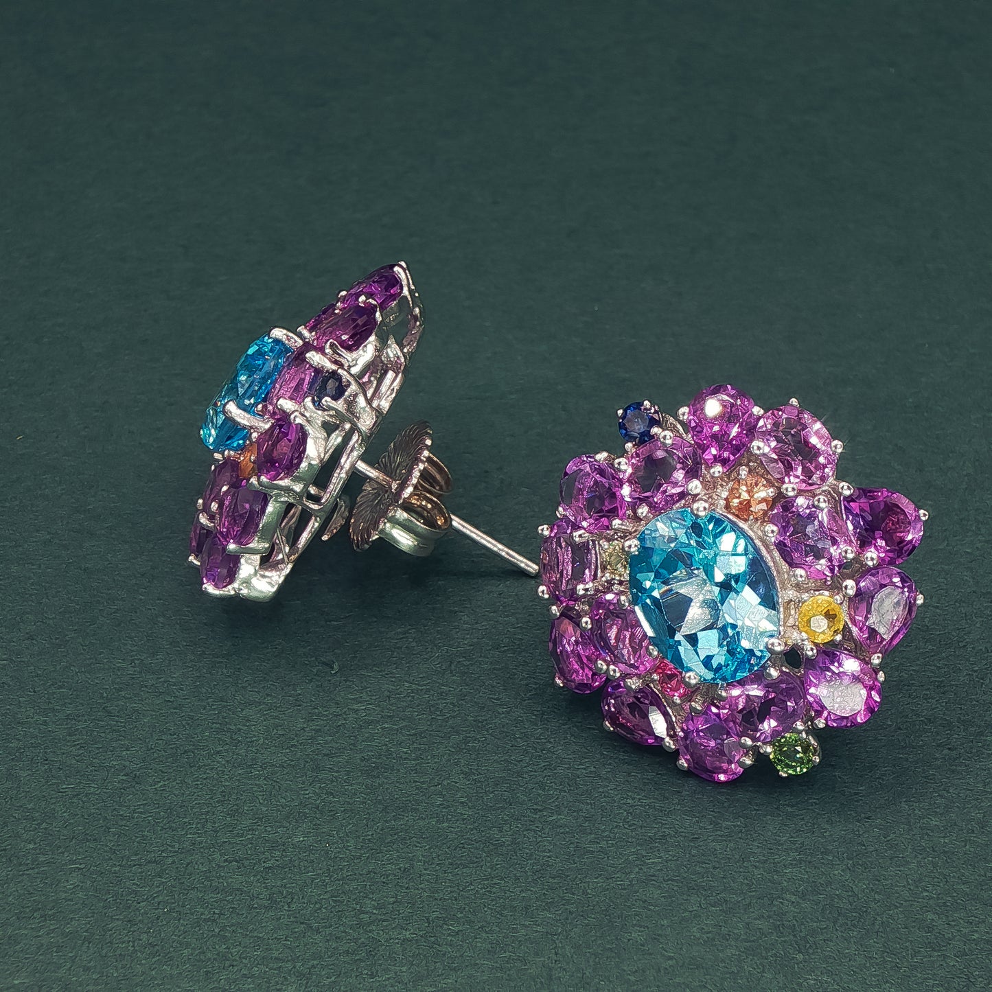 Colorful gemstone earrings on a dark green background

