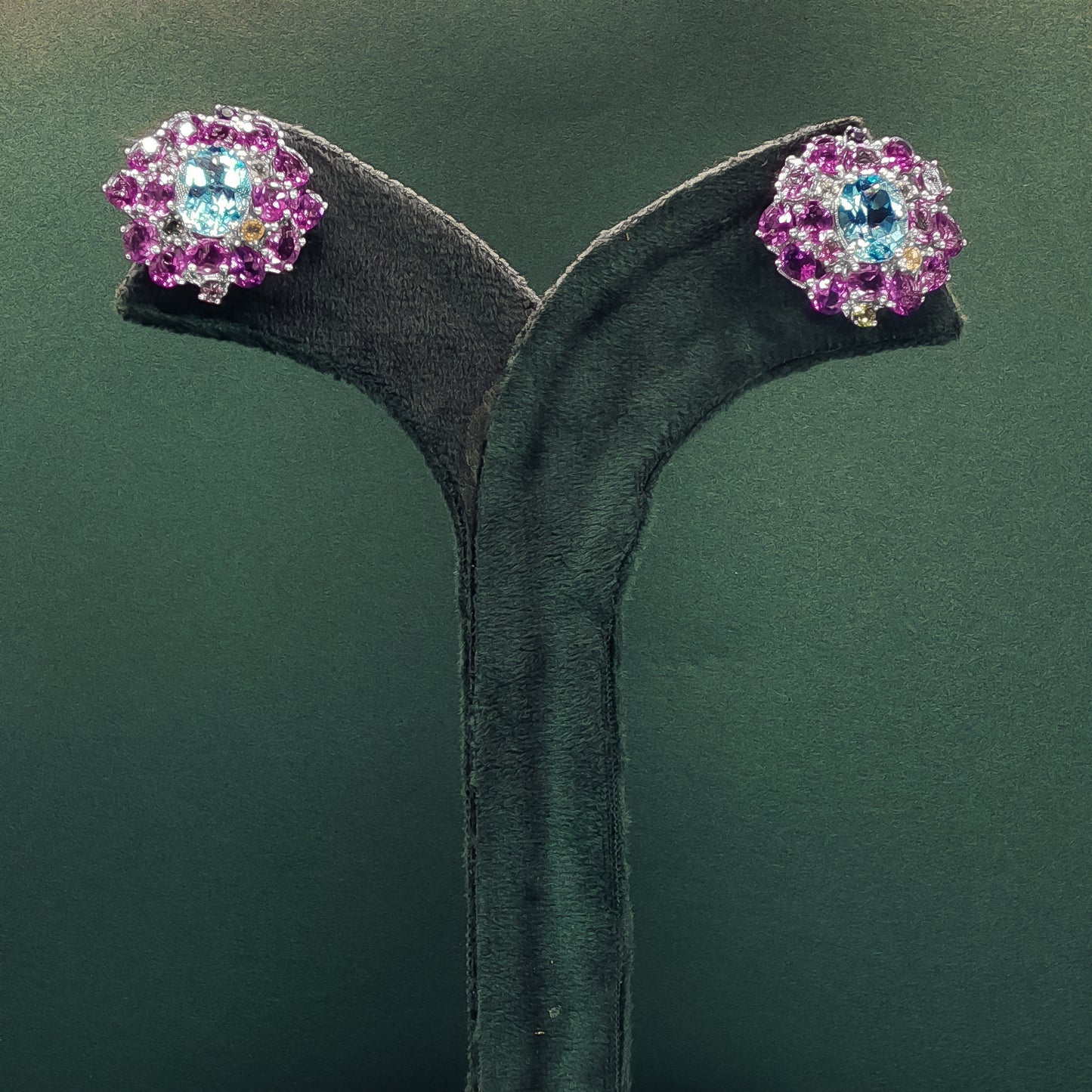 Pair of earrings with pink and blue gemstones on a green background


