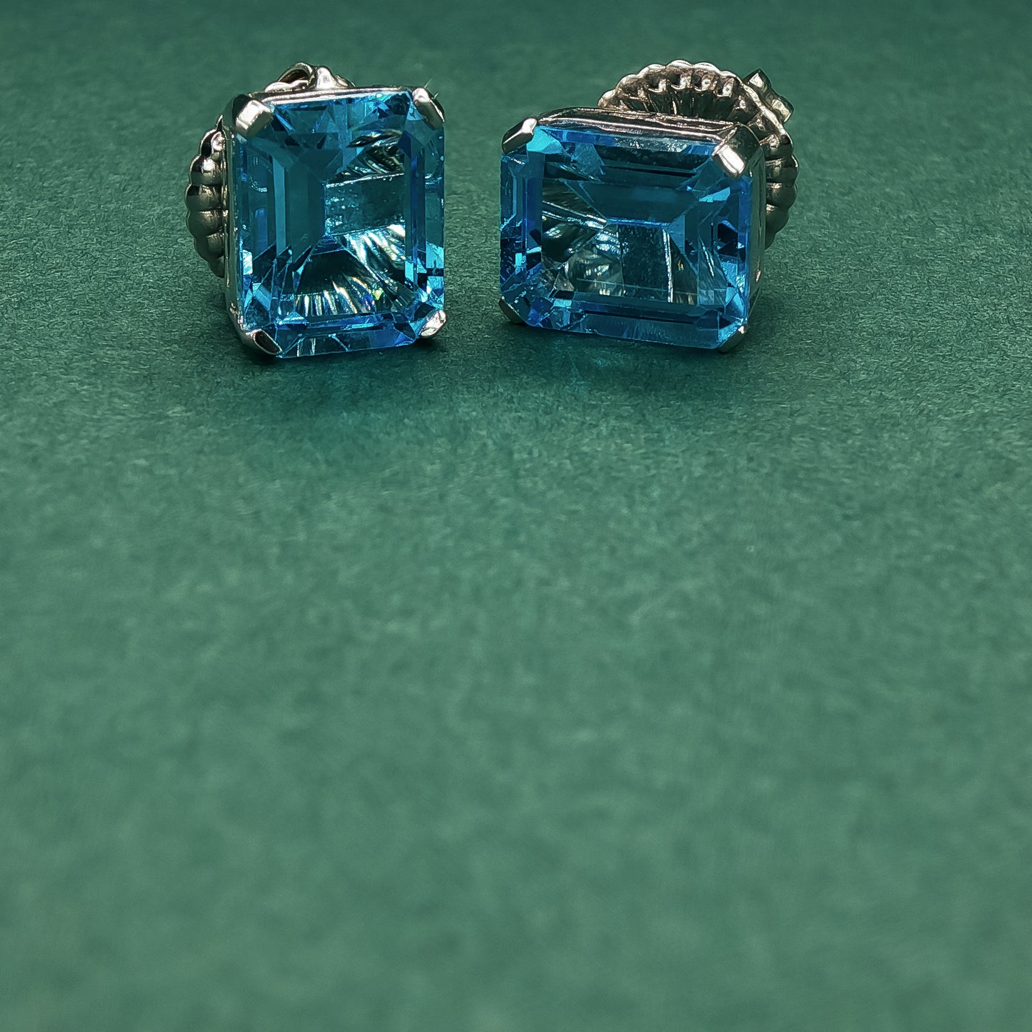 Pair of silver earrings with blue gemstones on a green background

