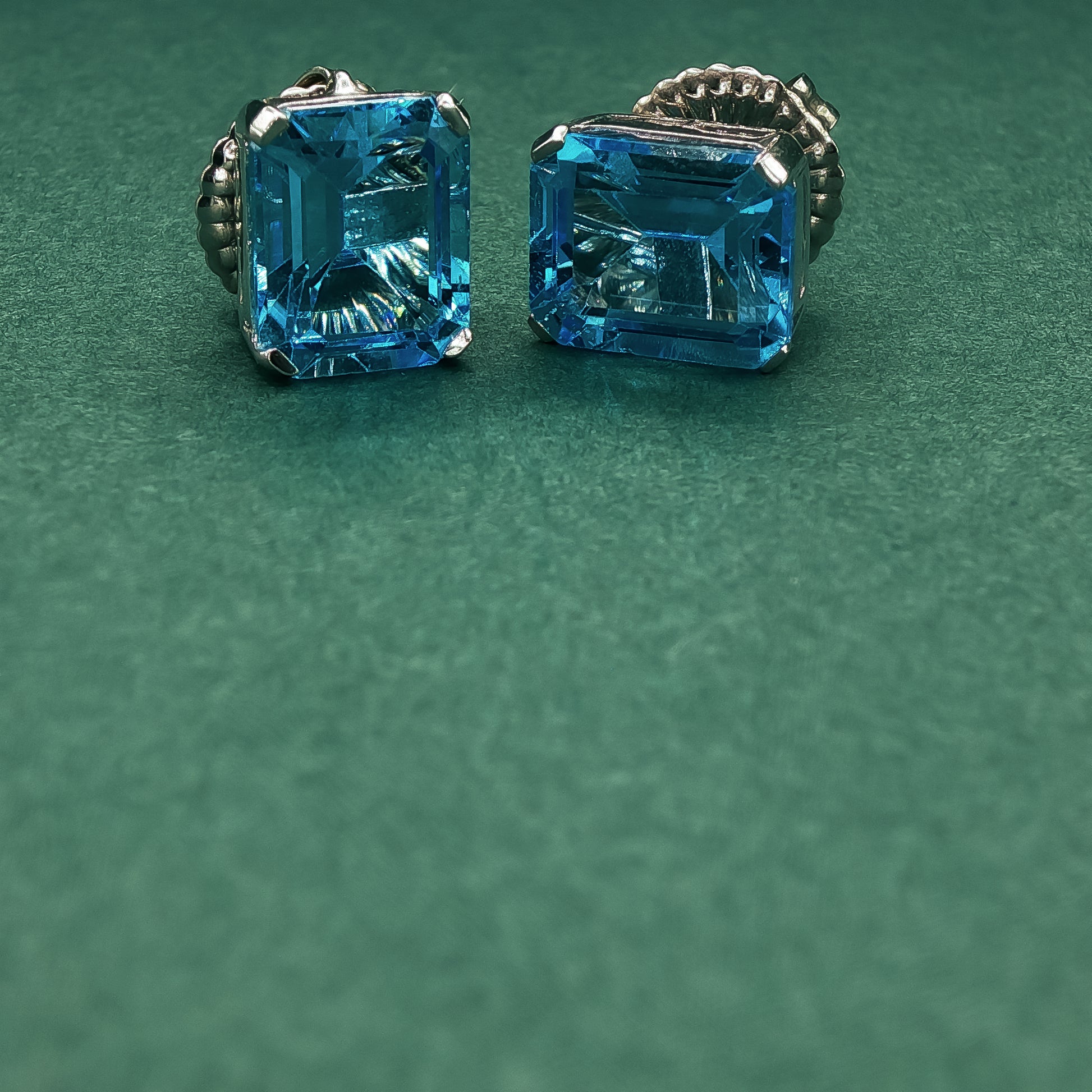 Pair of silver earrings with blue gemstones on a green background

