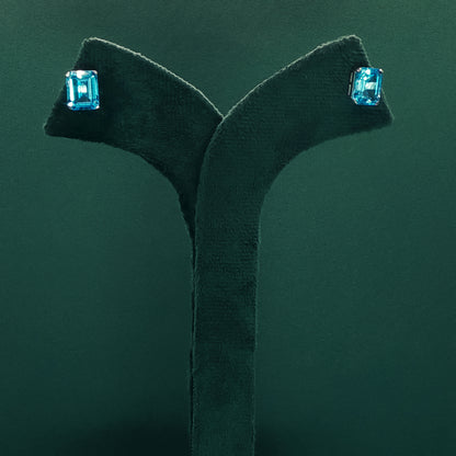 Blue gemstone earrings on a dark green stand against a matching background

