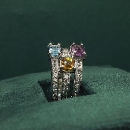 Three diamond-studded rings with colored gemstones on a green surface