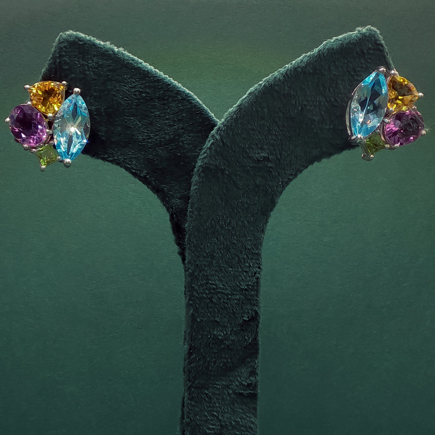 Multicolored gemstone earrings on a green stand against a dark green background