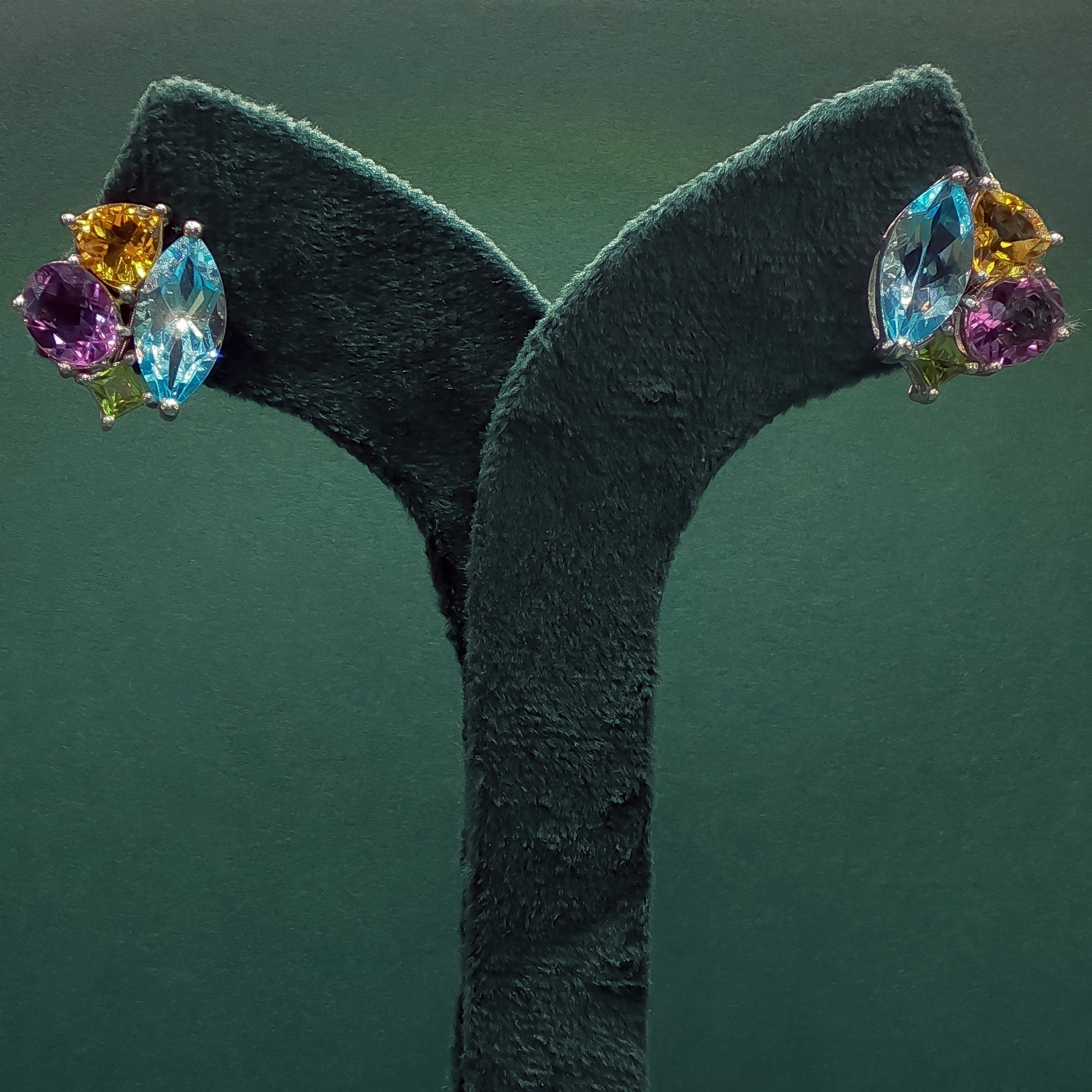 Multicolored gemstone earrings on a green stand against a dark green background