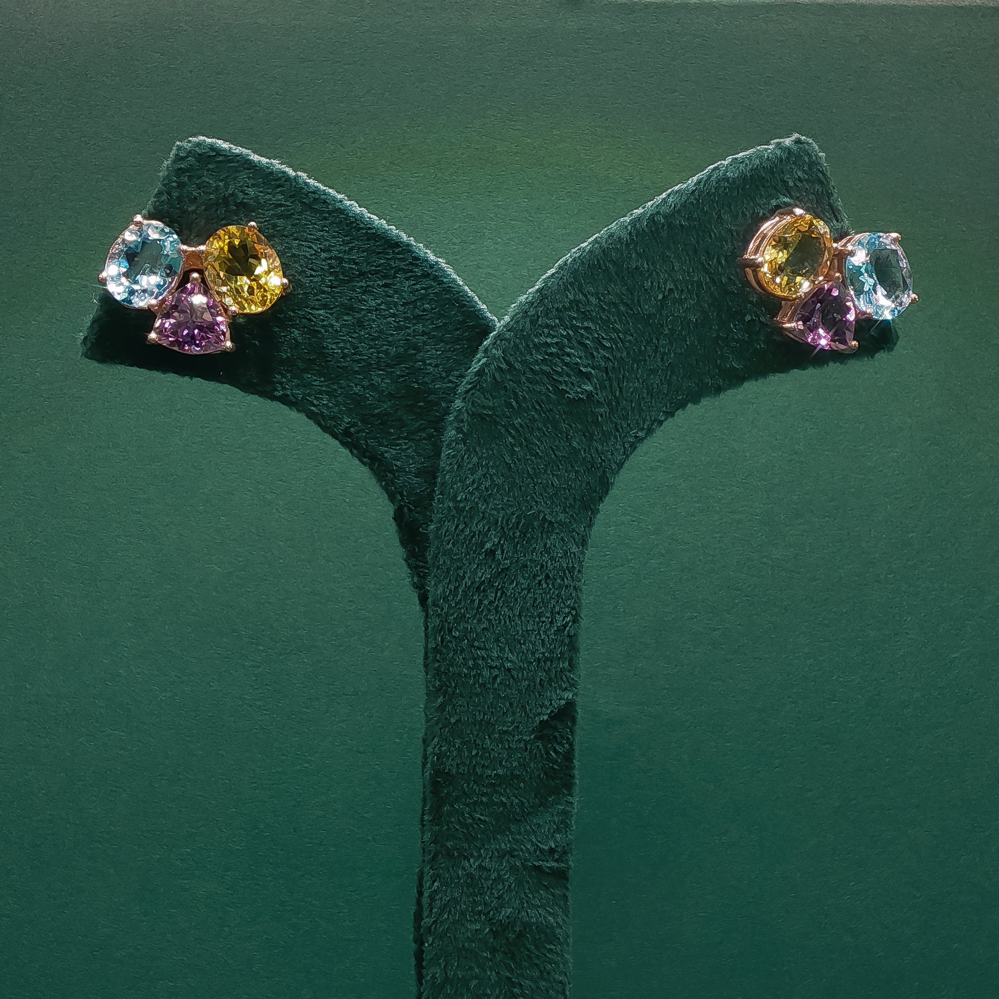 Colorful gemstone earrings on a green stand against a green background