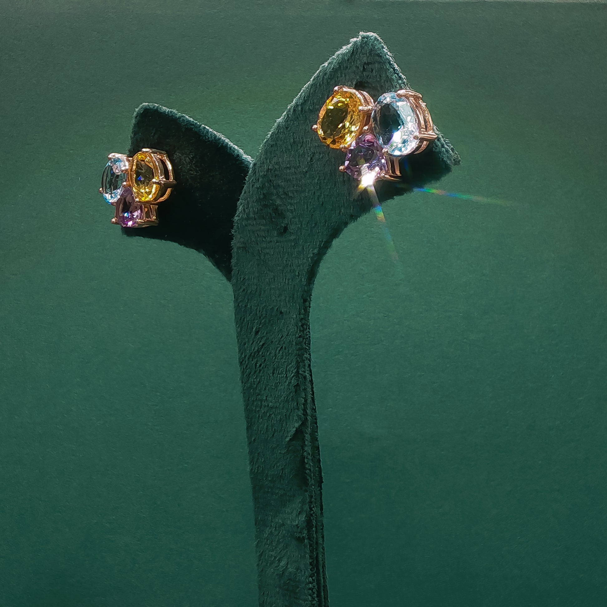 Pair of earrings with multicolored gemstones on a green stand against a green background