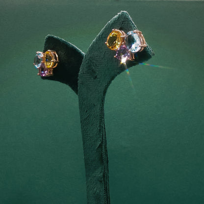 Pair of earrings with multicolored gemstones on a green stand against a green background