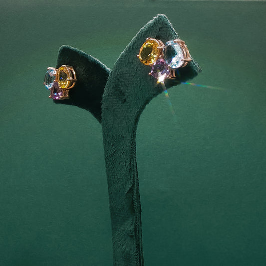 Pair of earrings with multicolored gemstones on a green stand against a green background