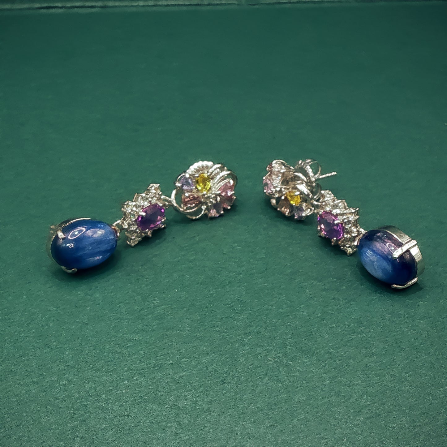 Pair of silver earrings with gemstones on a green background
