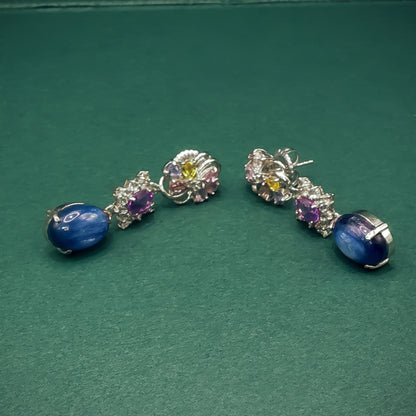 Pair of silver earrings with gemstones on a green background
