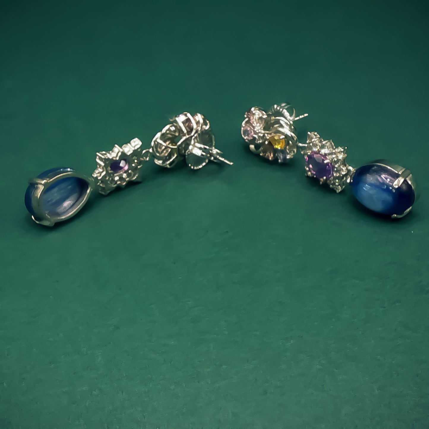 Pair of silver earrings with gemstones on a green background