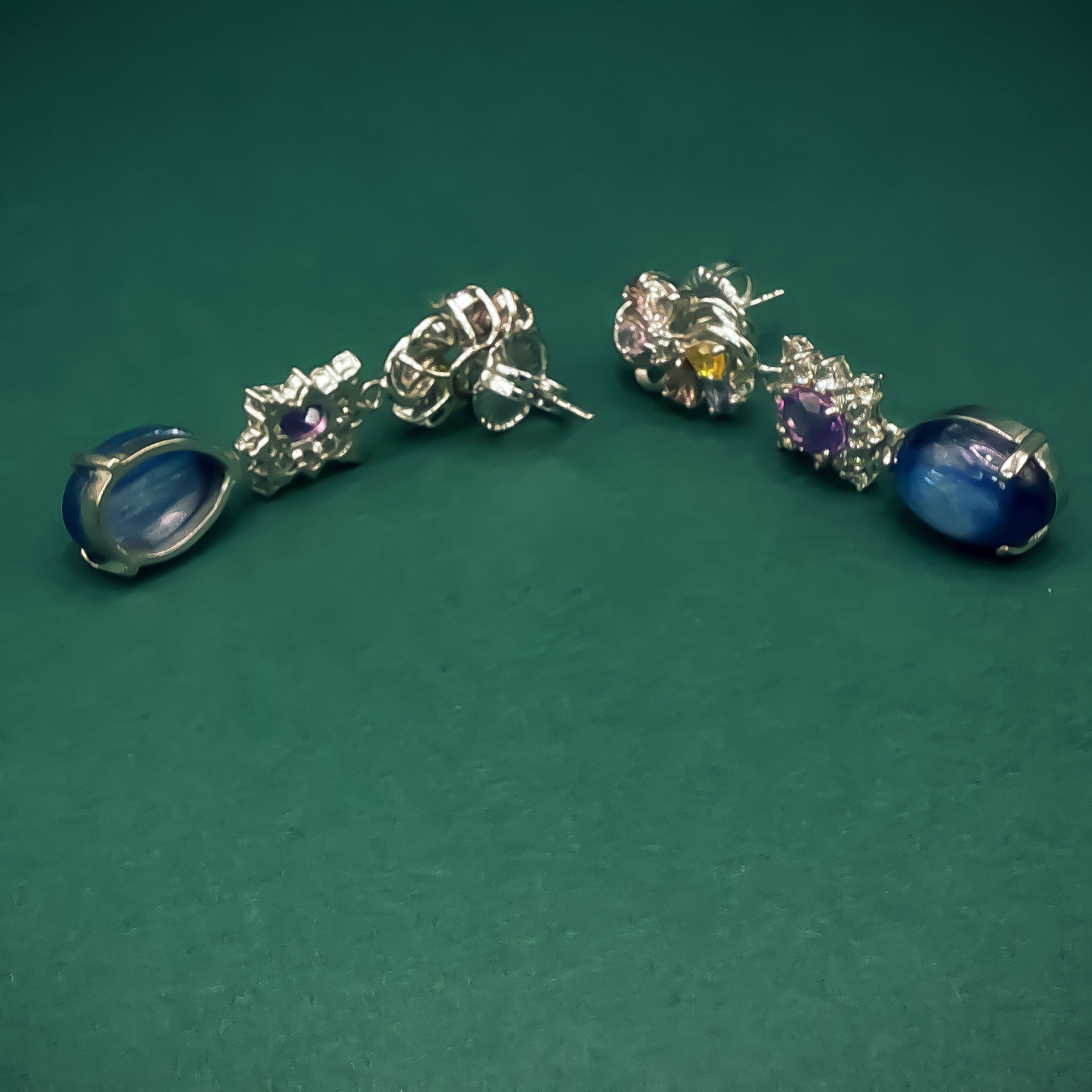Pair of silver earrings with gemstones on a green background