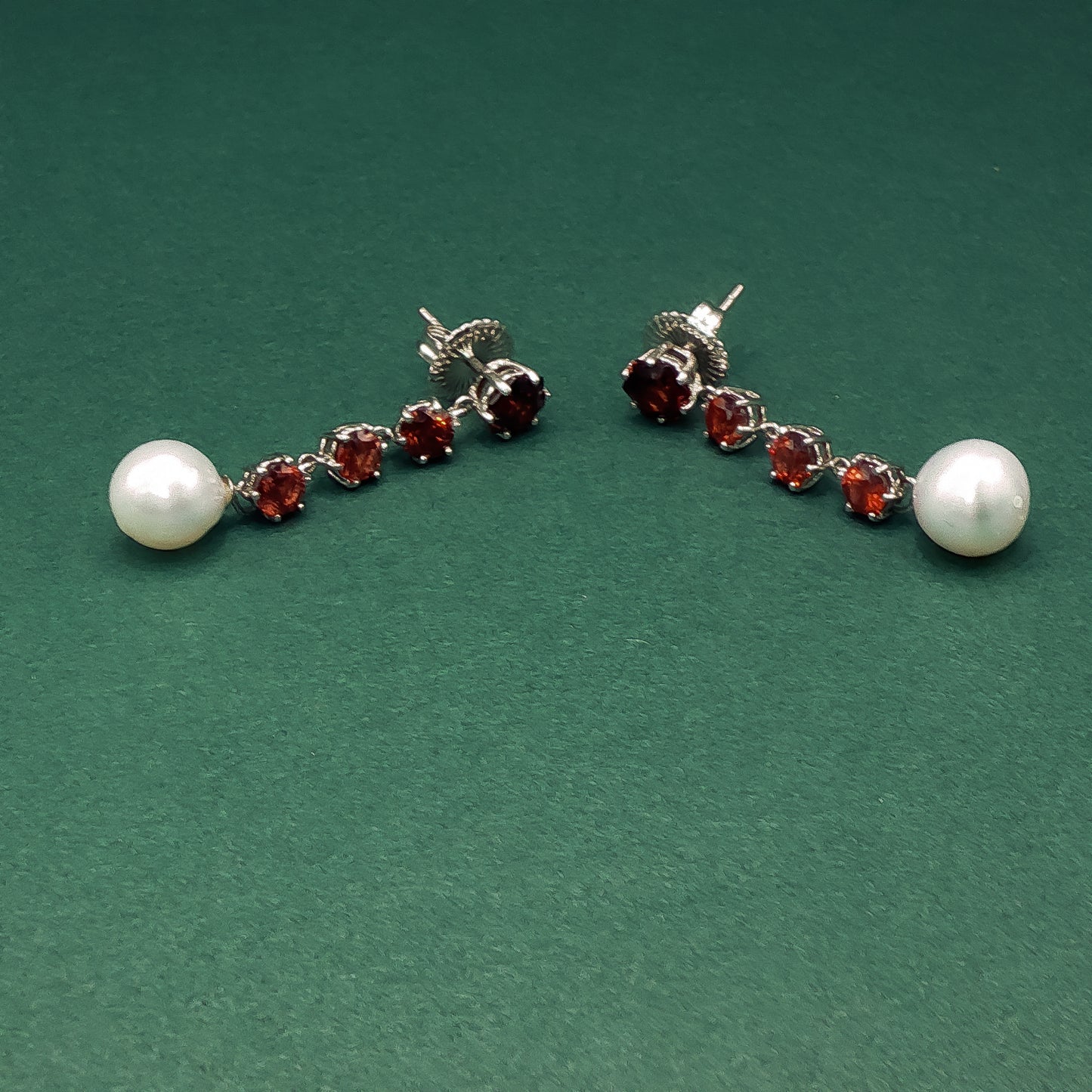 Pair of earrings with pearls and red gemstones on a green background