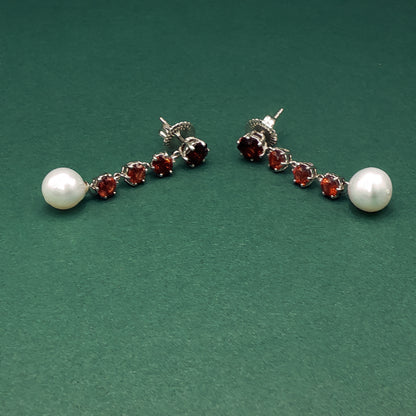 Pair of earrings with pearls and red gemstones on a green background