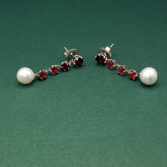 Pair of earrings with pearls and red gemstones on a green background