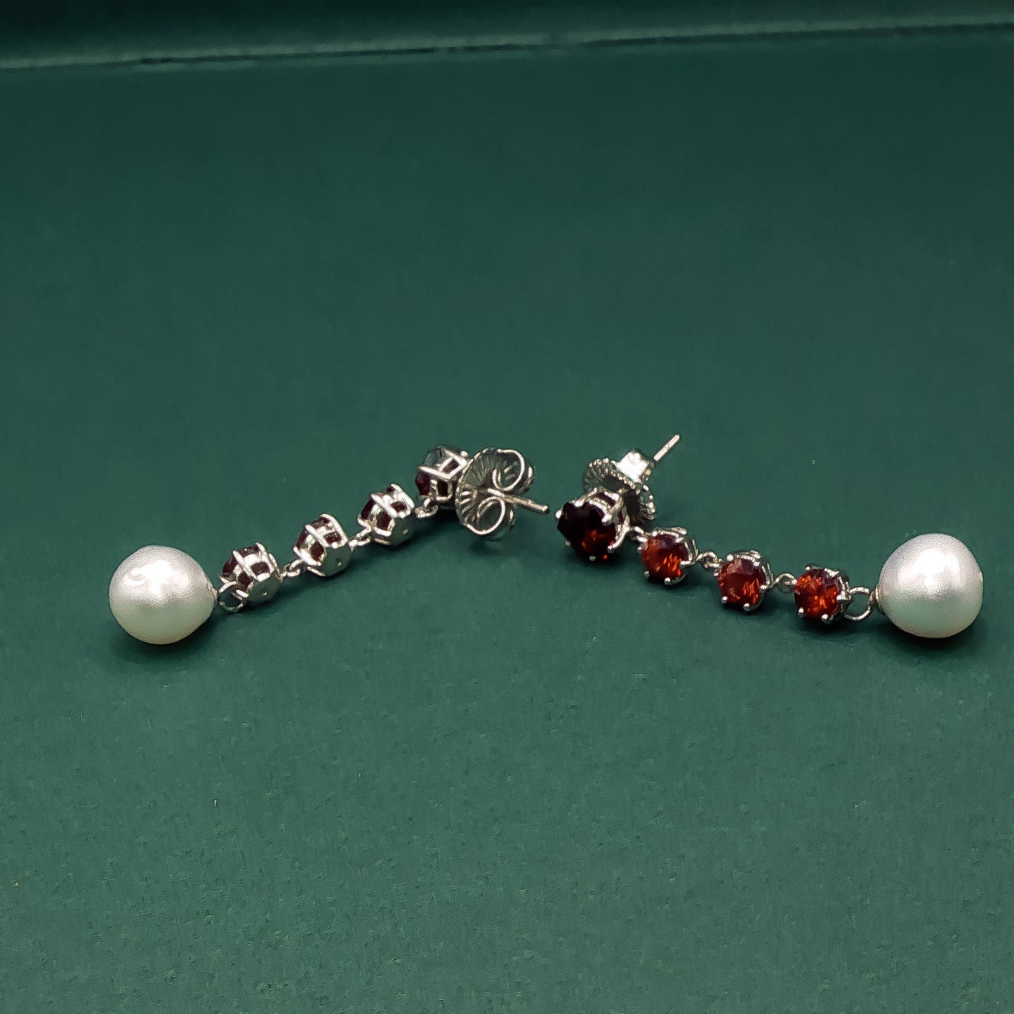 Pair of earrings with pearls and red gemstones on a green background