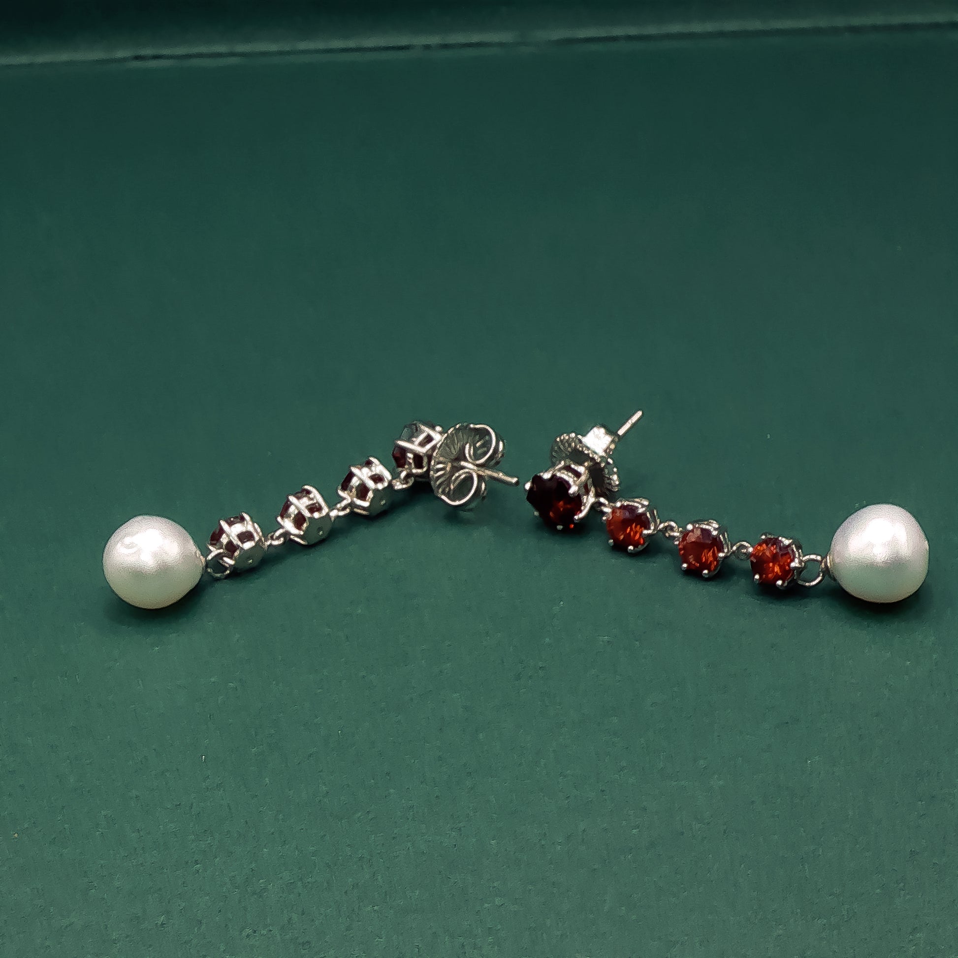 Pair of earrings with pearls and red gemstones on a green background