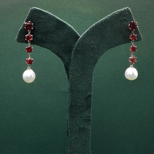Pair of earrings with pearls and red gemstones on a green stand.