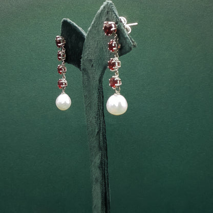 Pair of earrings with pearls and red gemstones on a green stand.
