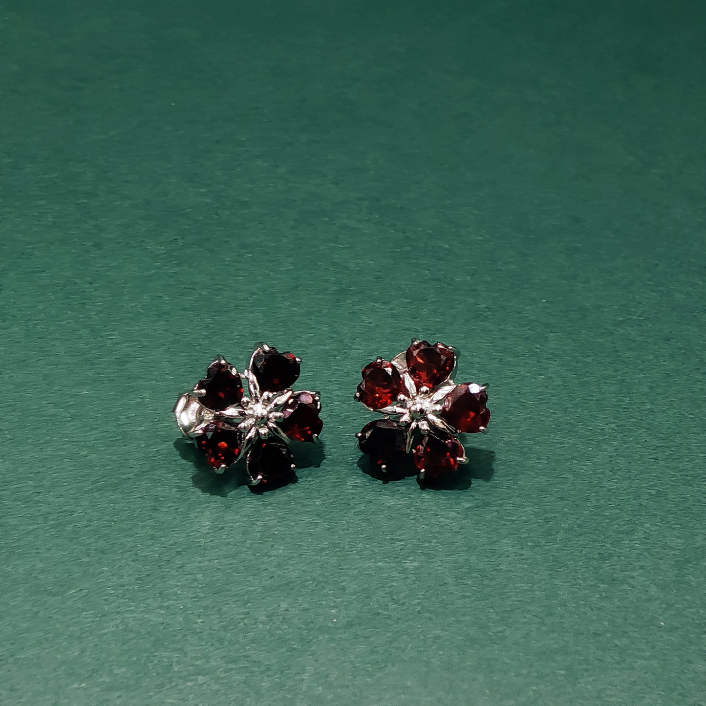 Pair of flower-shaped earrings with red gemstones on a green background
