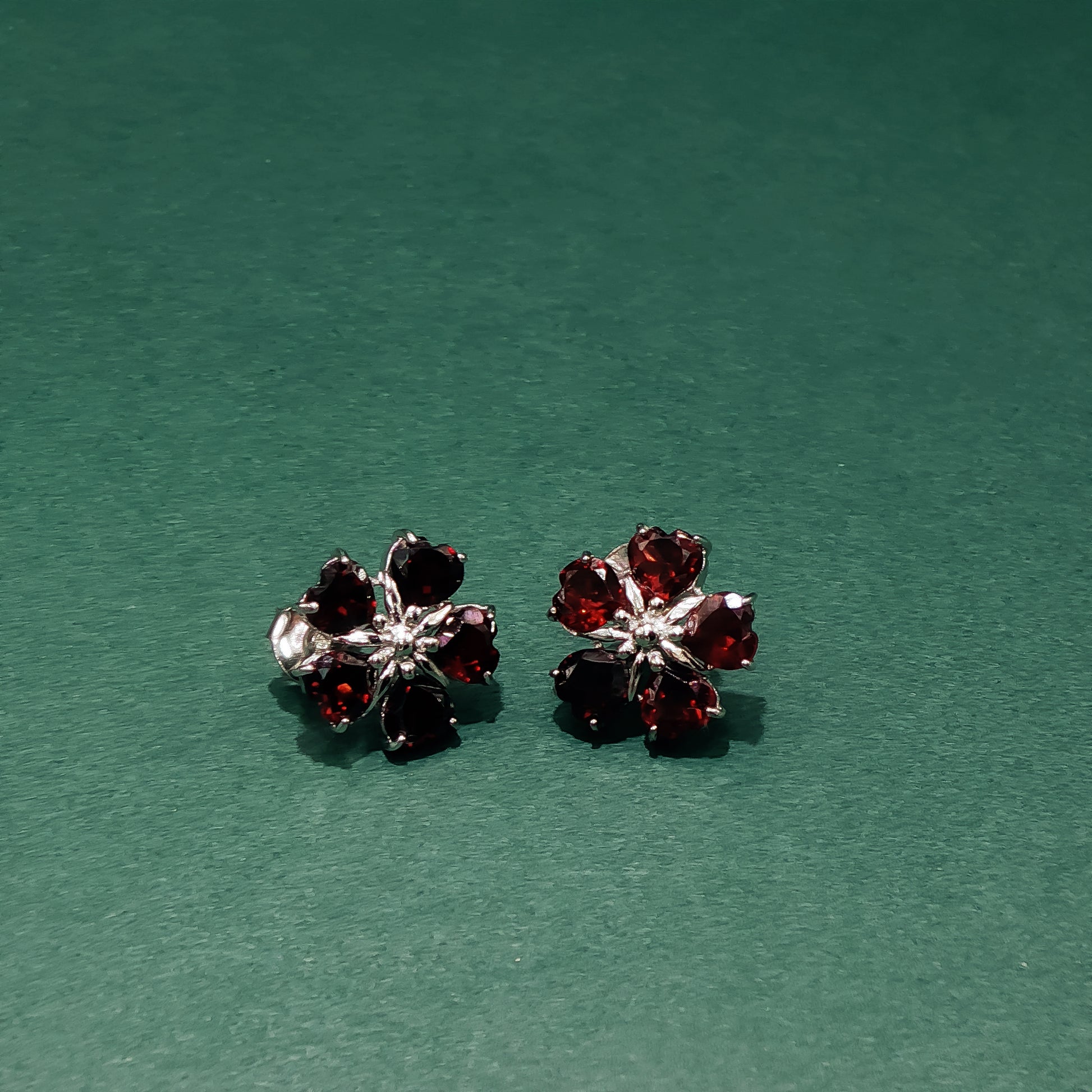 Pair of flower-shaped earrings with red gemstones on a green background