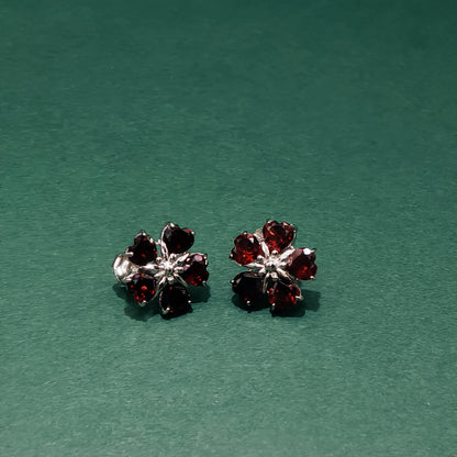 Pair of flower-shaped earrings with red gemstones on a green background
